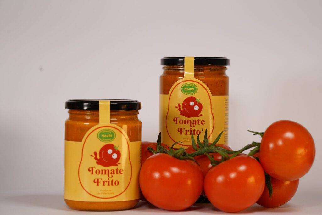 Tarros de tomate frito Hortalizas Mauri junto a tomates frescos en rama, fotografía de producto